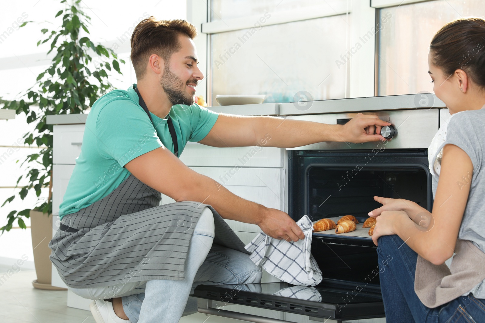 Photo of Young couple baking croissants in oven at home