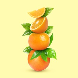 Stacked cut and whole oranges with green leaves on pale light yellow background