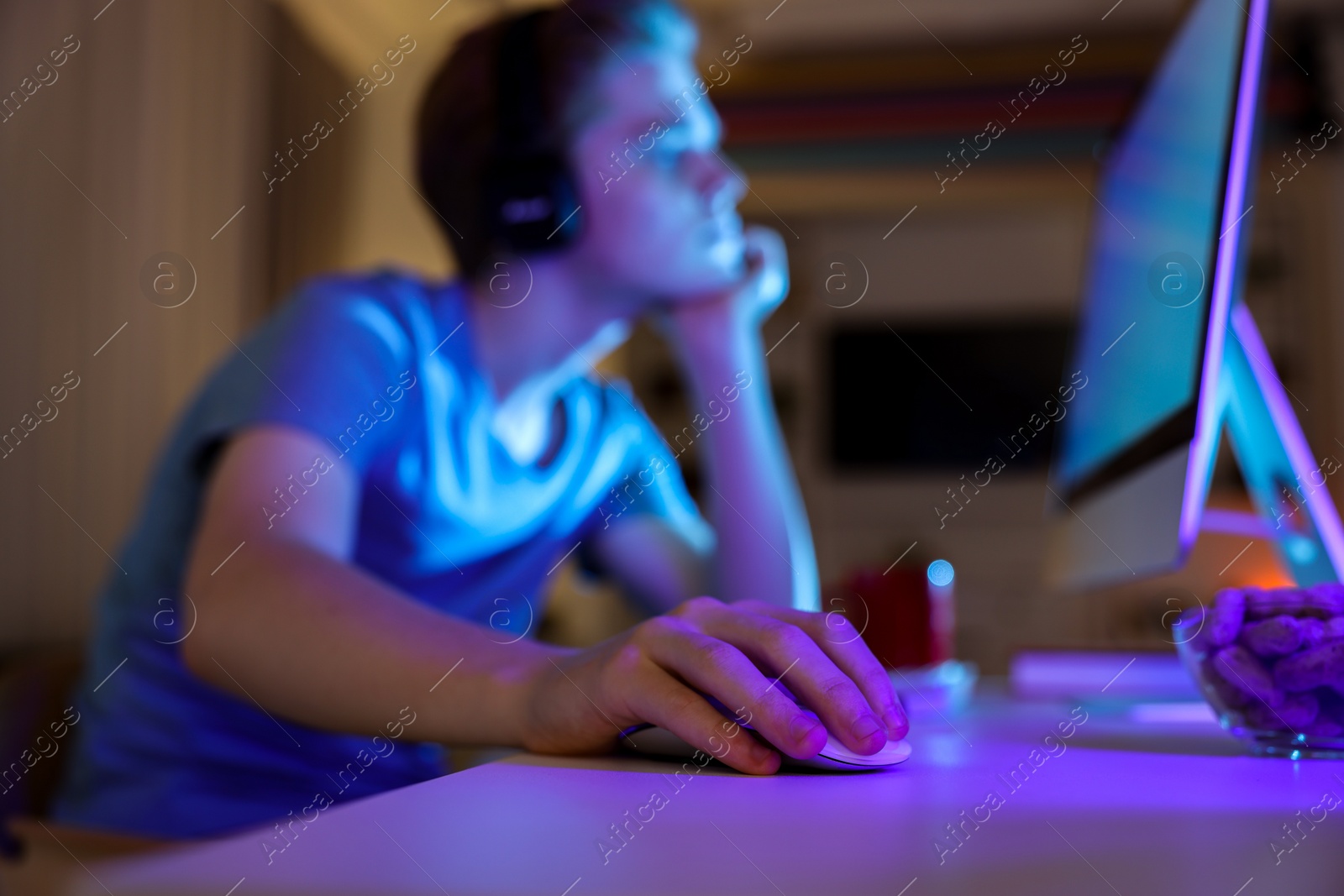 Photo of Teenage boy using computer in room at night, focus on hand. Internet addiction