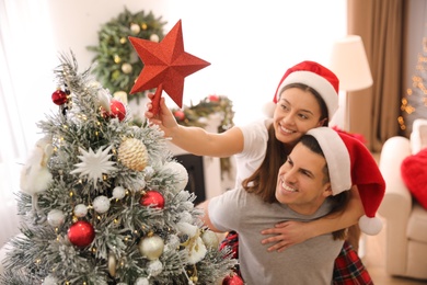 Couple decorating Christmas tree indoors, focus on star topper
