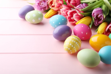 Bright painted eggs and spring tulips on pink wooden table, space for text. Happy Easter