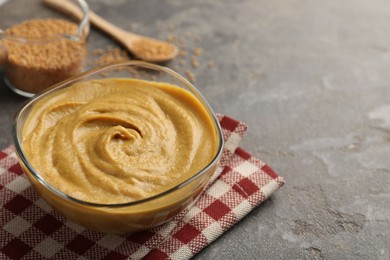 Photo of Tasty mustard sauce in glass bowl on grey textured table, space for text