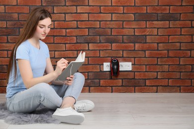 Woman reading book while charging electric heater indoors, space for text