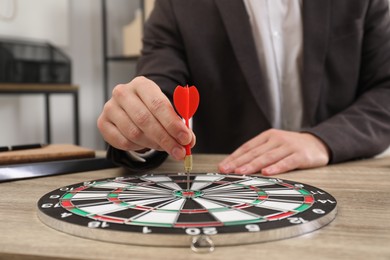 Business targeting concept. Man with dart aiming at dartboard at wooden table indoors, closeup