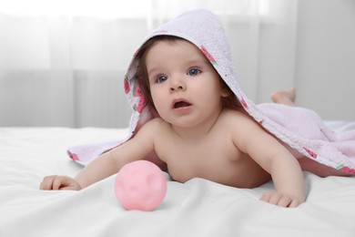 Photo of Cute little baby in hooded towel after bathing playing with toy on bed at home