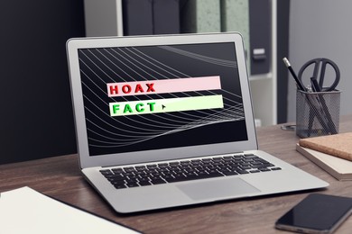Image of Choosing between hoax and fact. Laptop with words on wooden table in office