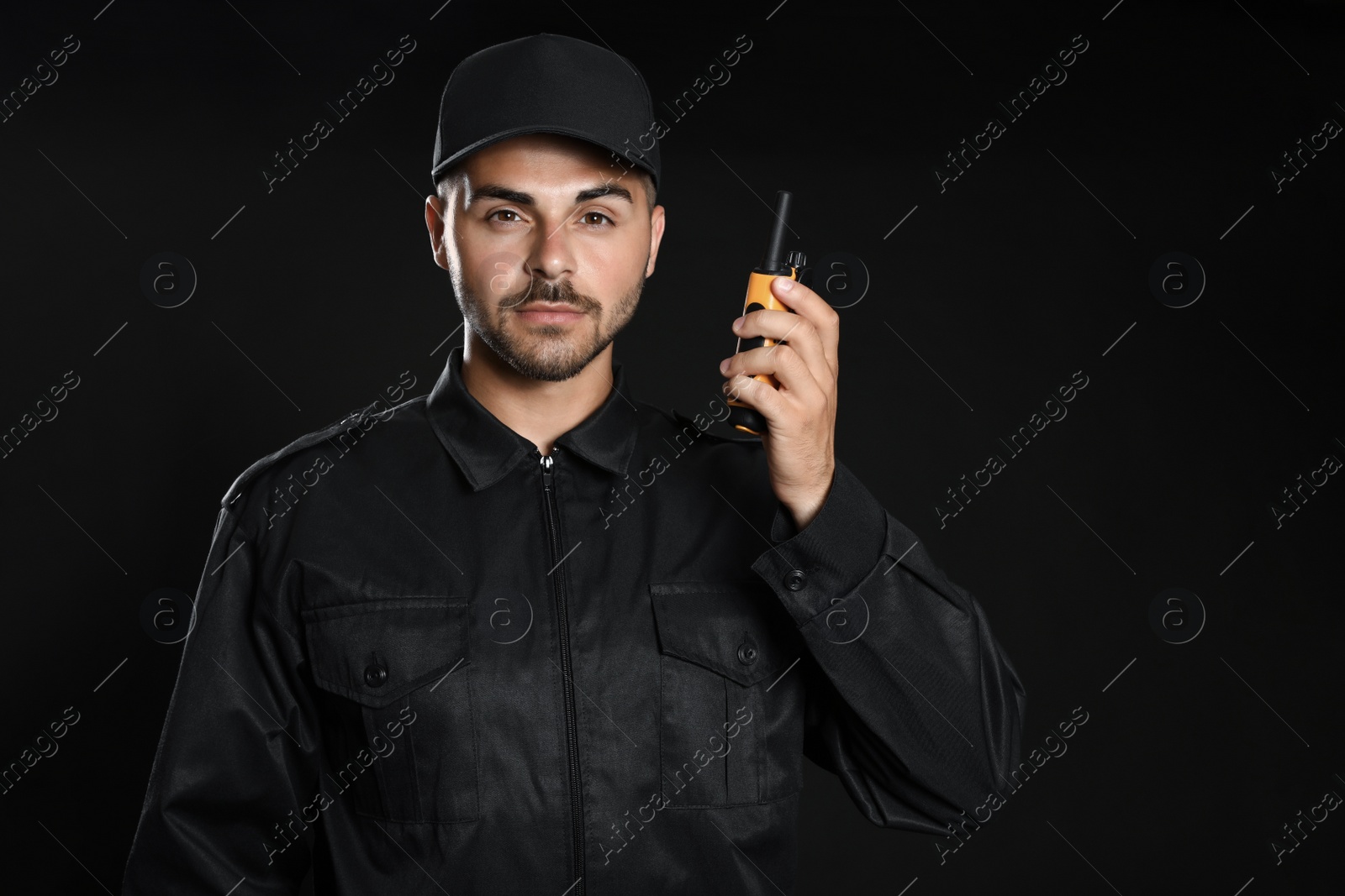 Photo of Male security guard in uniform using portable radio transmitter on dark background