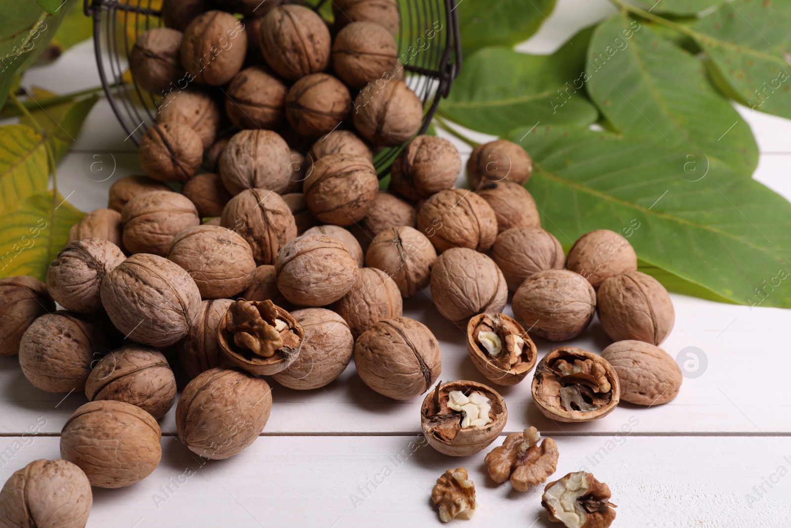 Photo of Pile of ripe walnuts and fresh leaves on white wooden table