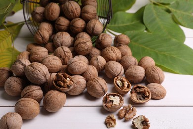 Pile of ripe walnuts and fresh leaves on white wooden table