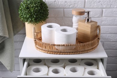 Photo of Toilet paper rolls, floral decor, dispenser and cotton pads on chest of drawers indoors