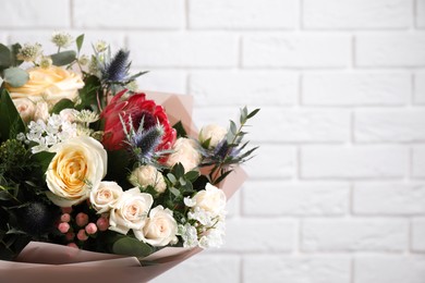 Beautiful bouquet with roses near white brick wall, closeup. Space for text