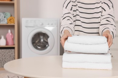 Woman with stack of folded towels at white table in laundry room, closeup. Space for text