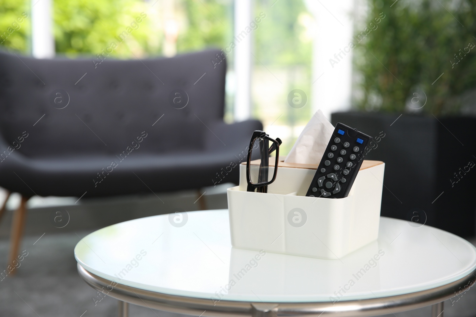 Photo of Box with paper tissues, glasses and TV remote control on white table in living room. Space for text