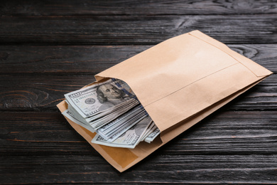 Envelope with dollar bills on black wooden table. Bribe concept