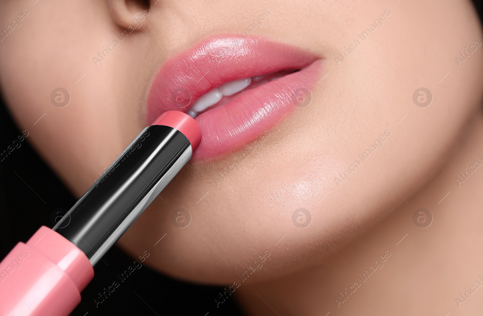 Photo of Closeup view of young woman applying beautiful nude lipstick