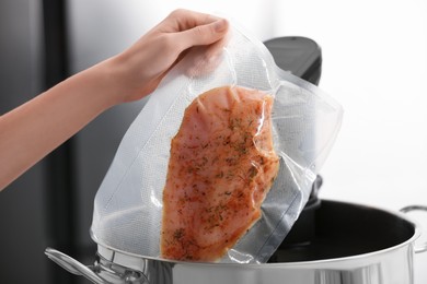 Photo of Woman putting vacuum packed meat into pot with sous vide cooker, closeup. Thermal immersion circulator