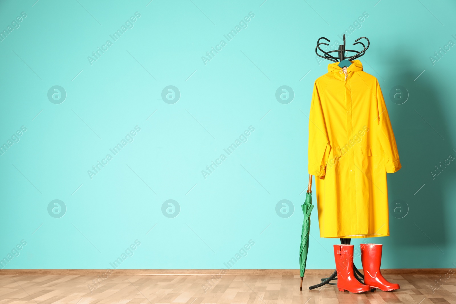 Photo of Umbrella, rain coat and boots near color wall with space for design