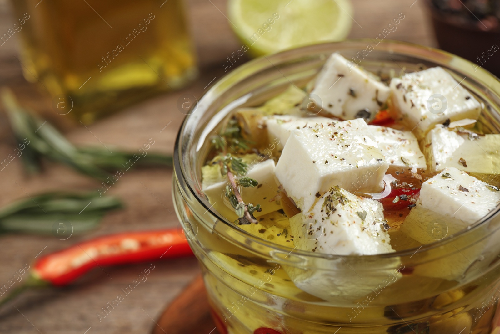 Photo of Glass jar of marinated feta cheese on wooden table, closeup