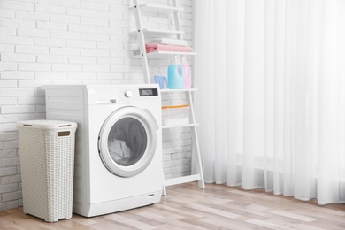 Modern washing machine near brick wall in laundry room interior, space for text