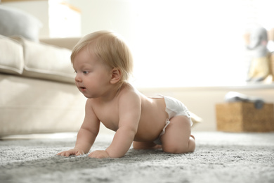 Cute little baby in diaper on carpet at home