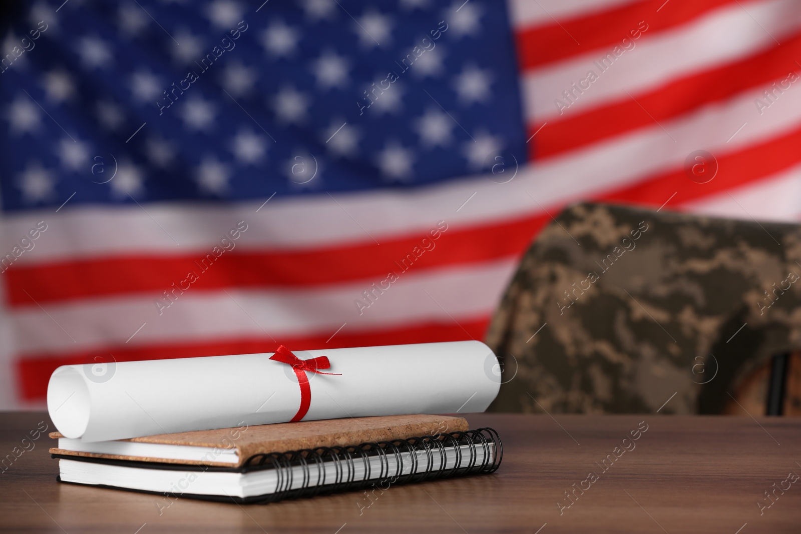 Photo of Diploma and notebooks on wooden table against flag of USA, space for text. Military education