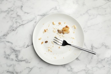 Photo of Dirty plate with food leftovers and fork on marble background, top view