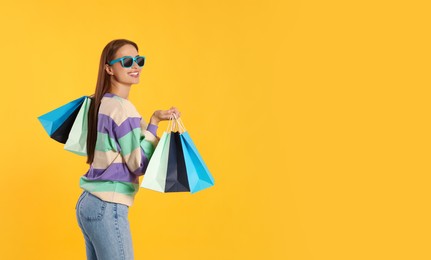Photo of Happy young woman with shopping bags on yellow background, space for text. Big sale