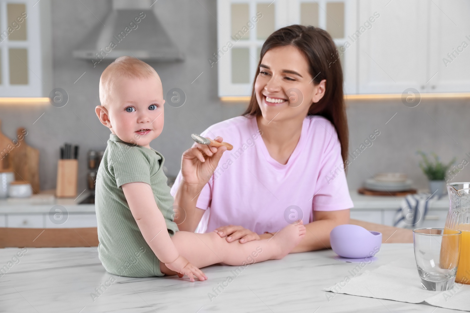 Photo of Happy young woman feeding her cute little baby at table in kitchen