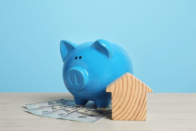 Photo of Piggy bank, house model and banknotes on white wooden table