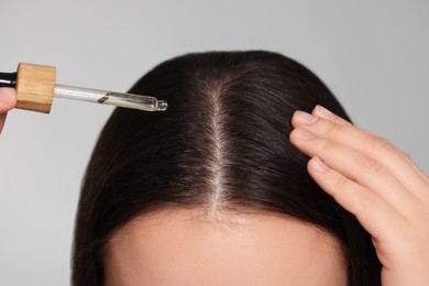 Photo of Woman applying essential oil onto hair on grey background, closeup