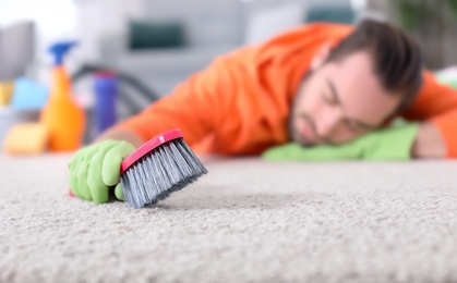 Tired man after cleaning carpet sleeping on floor at home