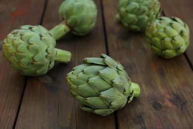 Photo of Whole fresh raw artichokes on wooden table, closeup