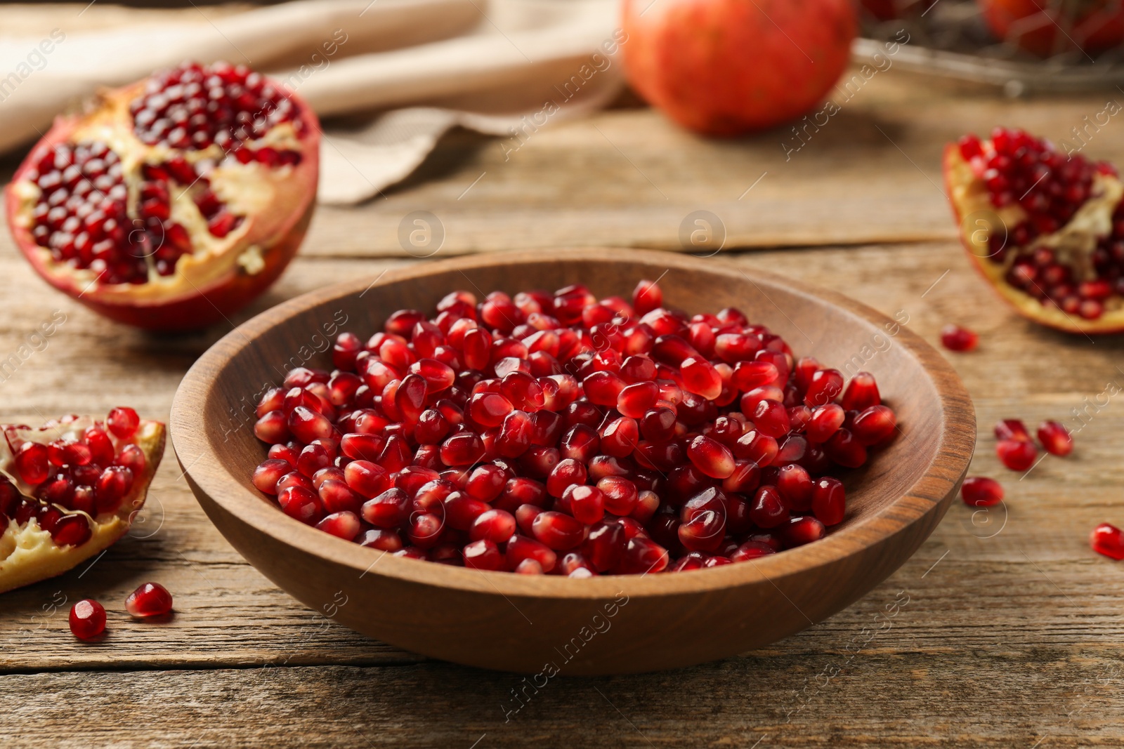 Photo of Ripe juicy pomegranate grains in bowl on wooden table, closeup