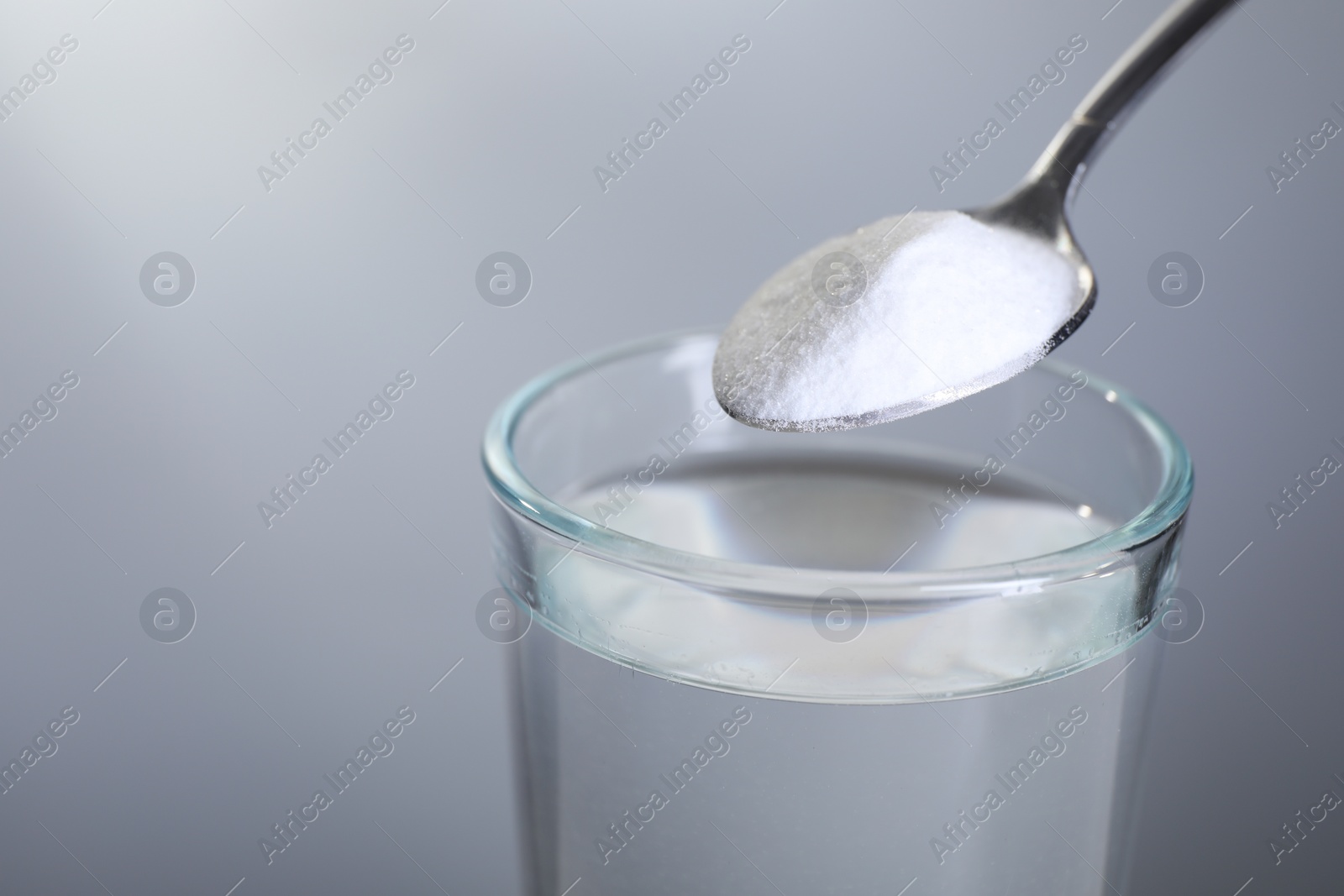 Photo of Spoon with baking soda over glass of water on light grey background, closeup. Space for text