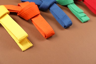 Photo of Colorful karate belts on brown background, closeup. Space for text