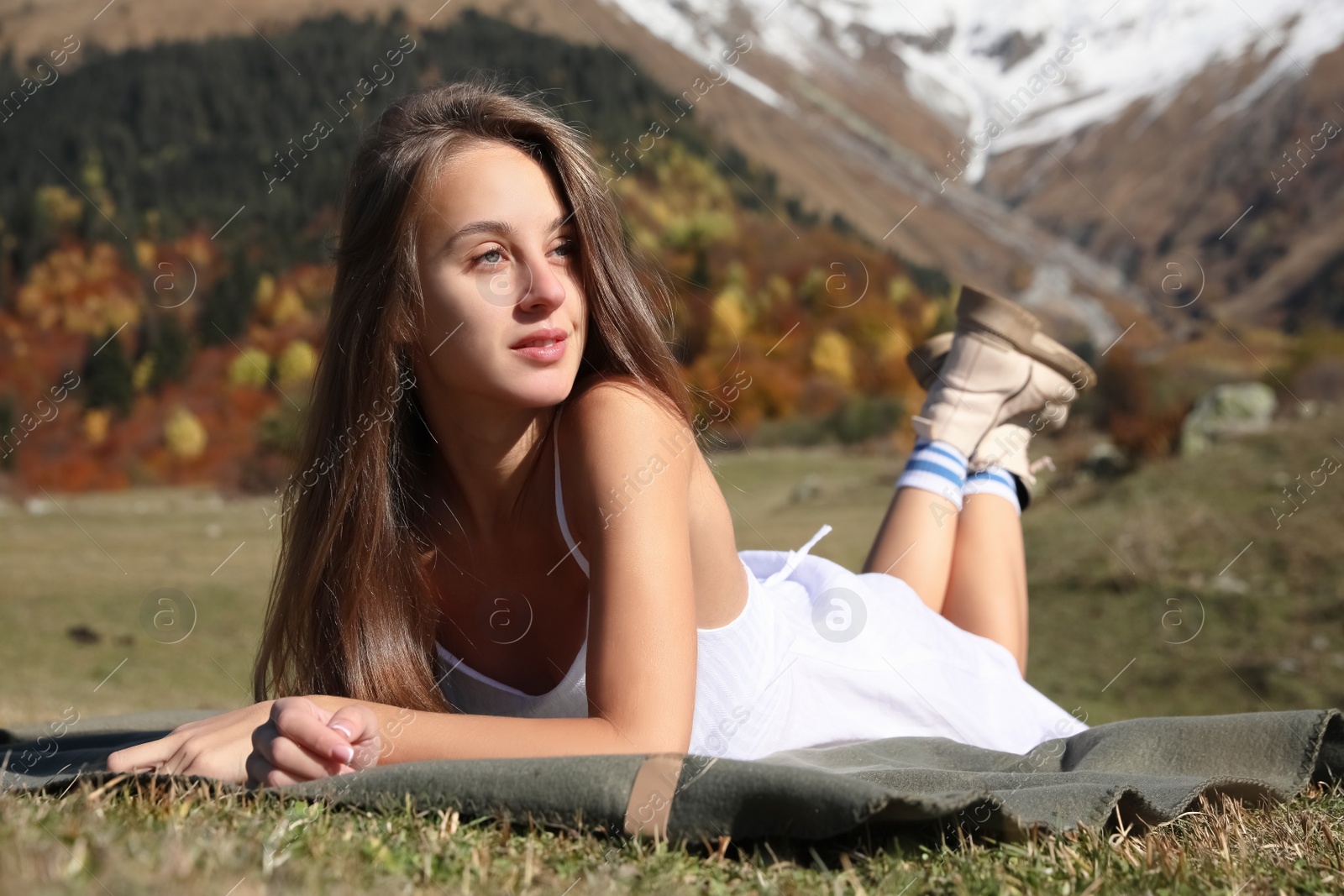 Photo of Beautiful young woman relaxing on blanket in mountains
