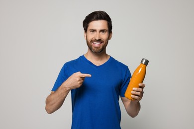 Photo of Man pointing at orange thermo bottle on light grey background