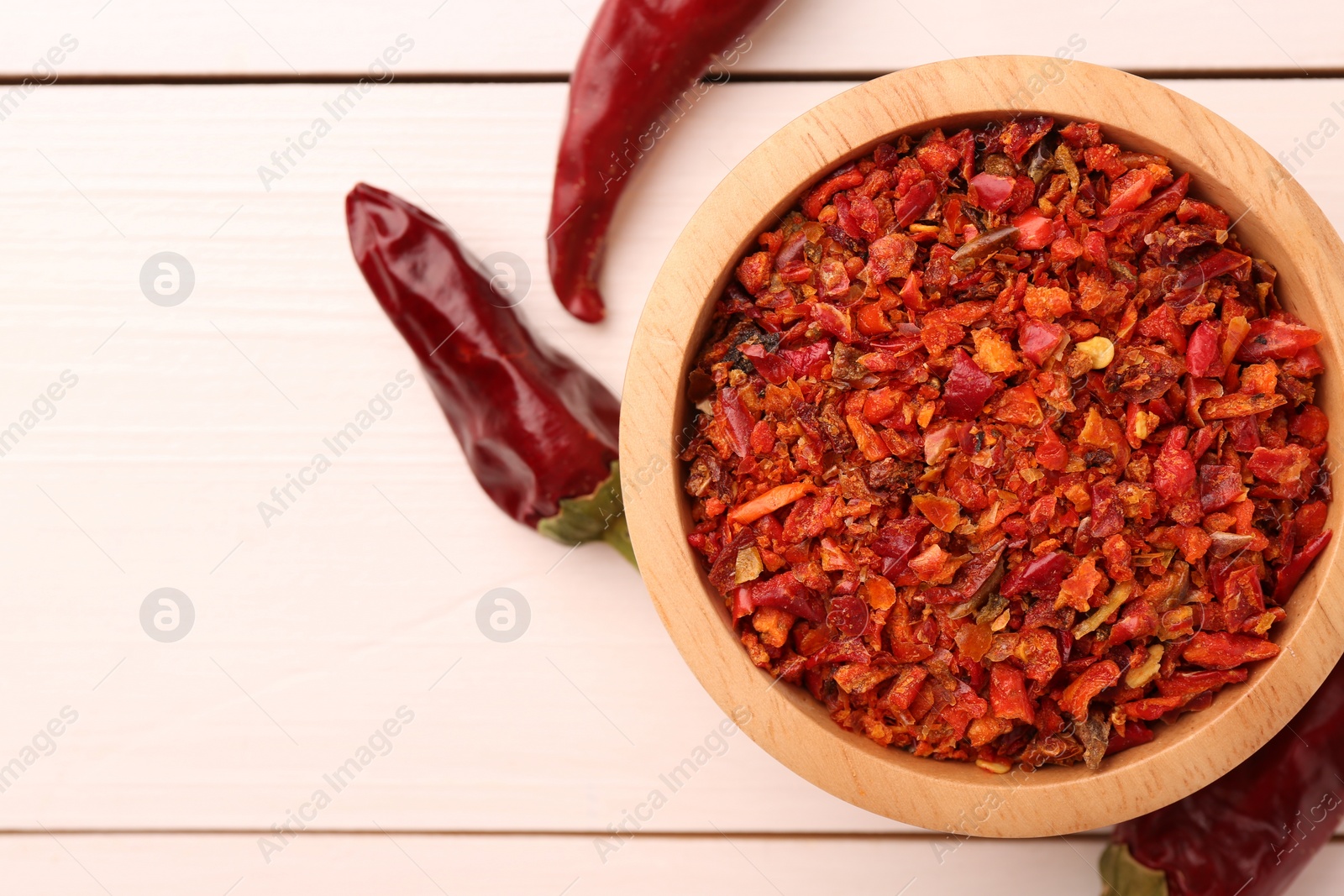 Photo of Chili pepper flakes in bowl and pods on white wooden table, flat lay. Space for text