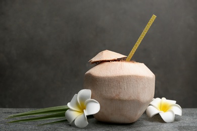 Photo of Young peeled coconut with straw, palm leaf and flowers on grey table. Space for text