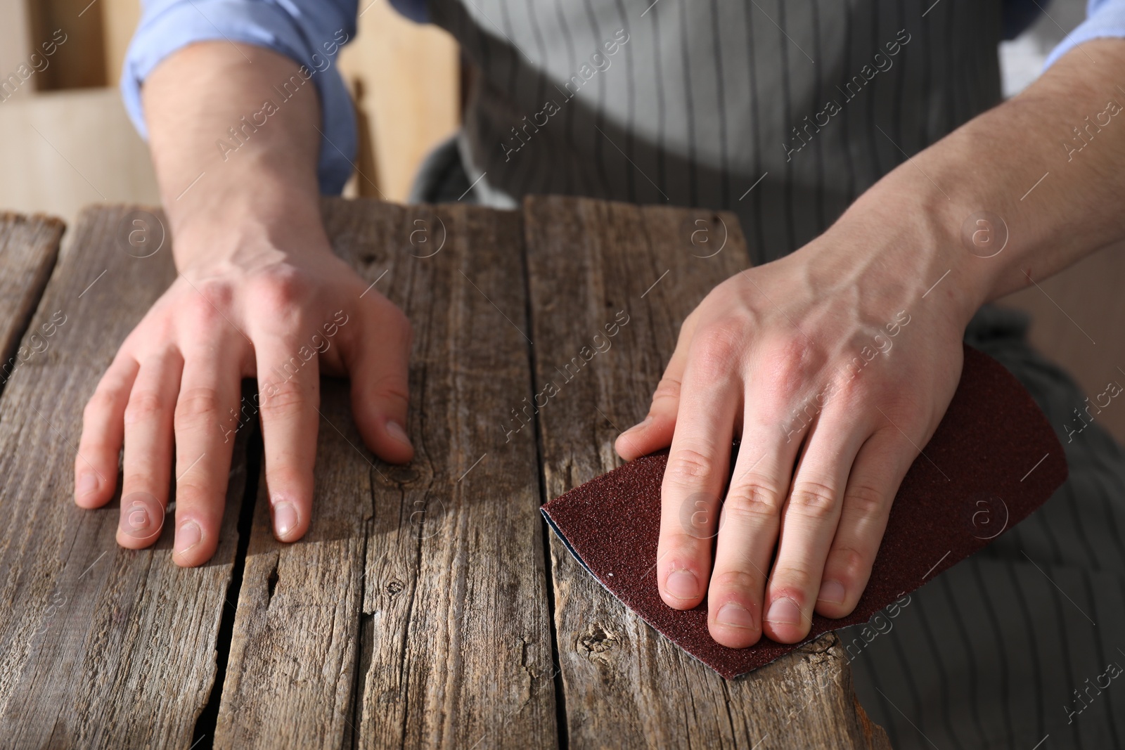 Photo of Man polishing wooden table with sandpaper indoors, closeup