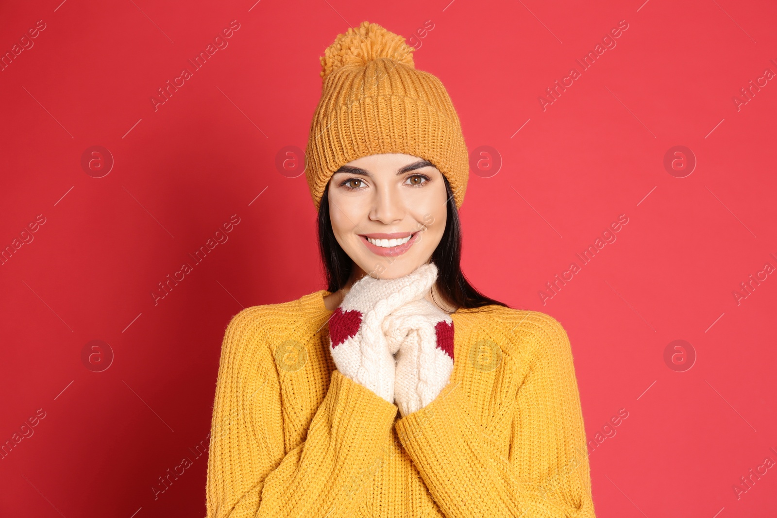 Photo of Young woman wearing warm sweater, mittens and hat on red background. Winter season