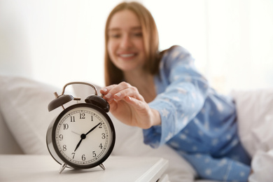Photo of Young woman turning off alarm clock at home in morning, focus on hand