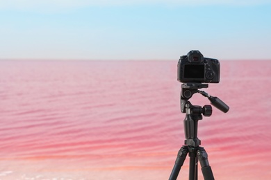 Professional camera on tripod near pink lake