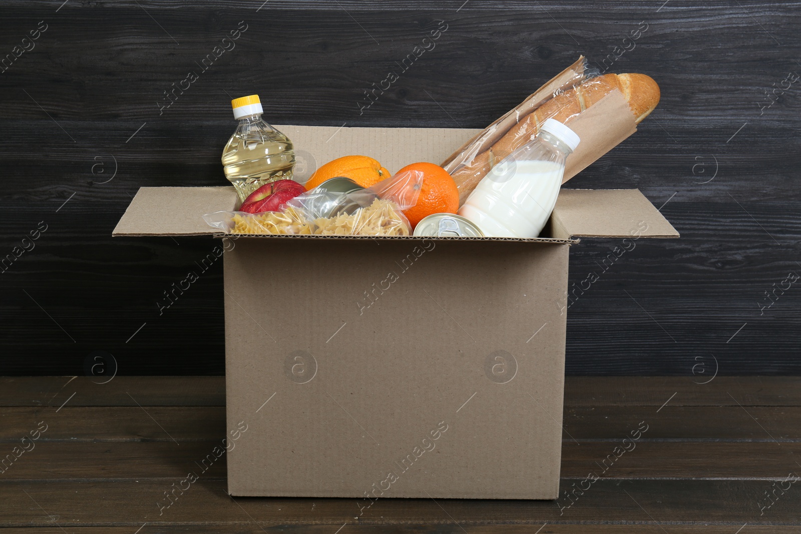 Photo of Cardboard box with donation food on wooden table, closeup