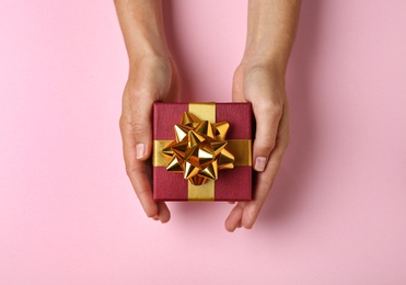 Woman holding beautiful gift box on pink background, top view