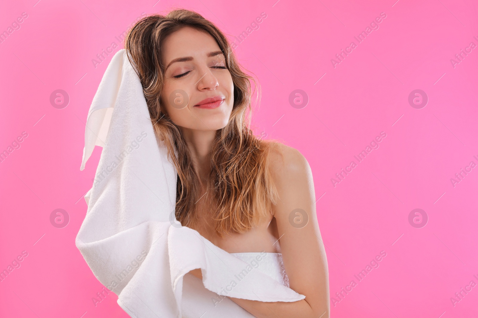 Photo of Beautiful young woman wiping hair with towel after washing on pink background