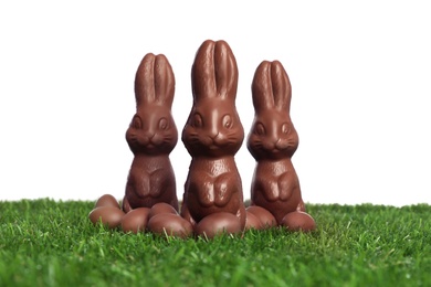 Chocolate bunnies and eggs on green grass against white background. Easter celebration