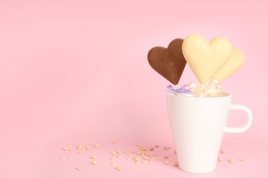 Photo of Different chocolate heart shaped lollipops in cup on light pink background. Space for text
