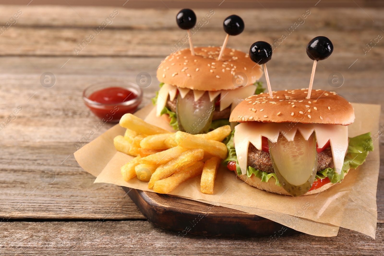 Photo of Cute monster burgers served with french fries and ketchup on wooden table, space for text. Halloween party food