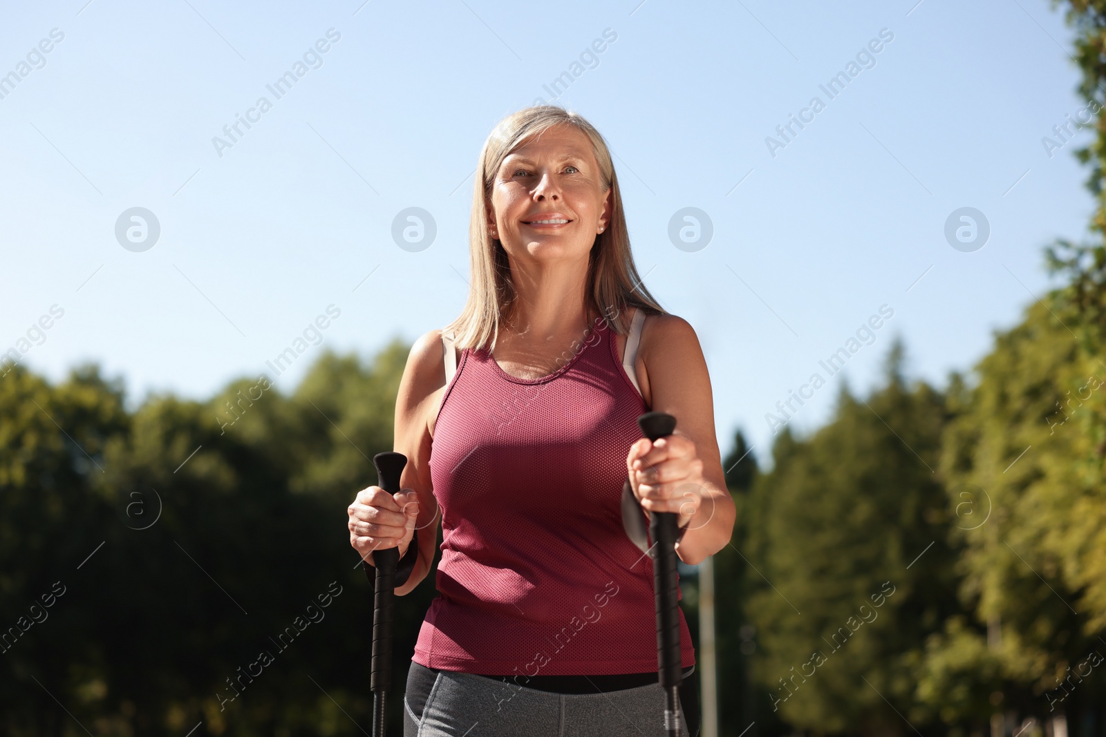 Photo of Woman practicing Nordic walking with poles outdoors on sunny day